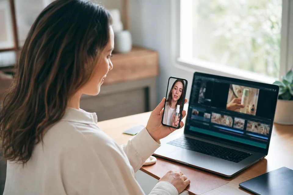 Marketer comparing a vertical presenter video ad on her phone with a stock-footage edit on her laptop