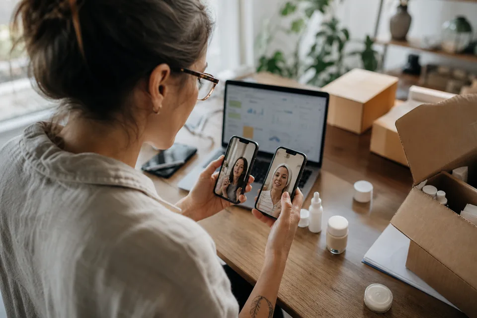 Performance marketer comparing several vertical talking-actor video ads on two phones at a desk with product samples