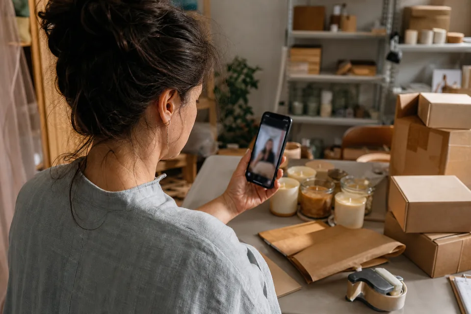 Small shop owner checking a vertical video ad on her phone behind the counter with parcels ready to ship